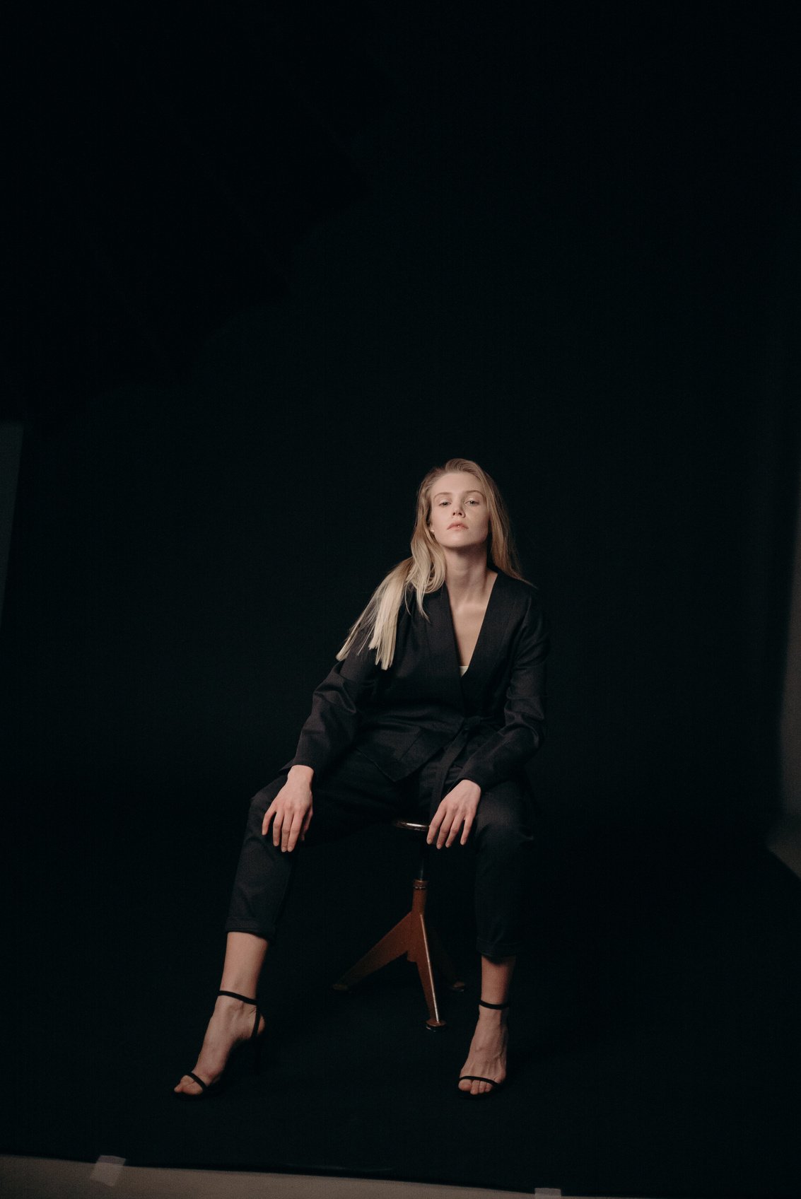 Woman in Black Blazer and Black Pants Sitting on Brown Wooden Stool